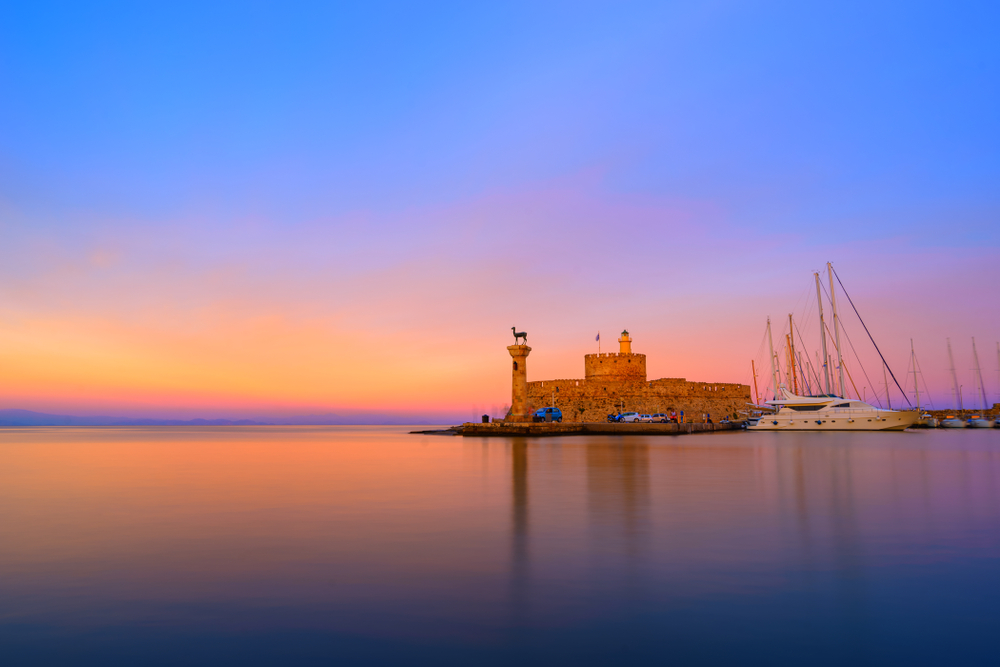 Hafen von Mandraki auf Rhodos mit Blick auf die Hafenmauer und Boote bei Sonnenuntergang