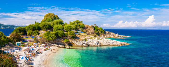 Bucht mit kleinem Badestrand mit Sonnenliegen auf Korfu mit Felsformation im Hintergrund