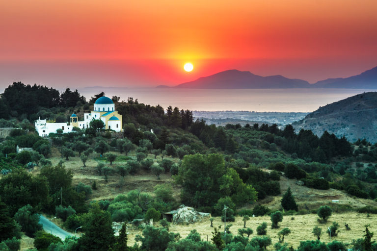Sonnenuntergang auf Kos mit typisch griechischer Kapelle im Vordergrund und Küstenlinie im Hintergrund