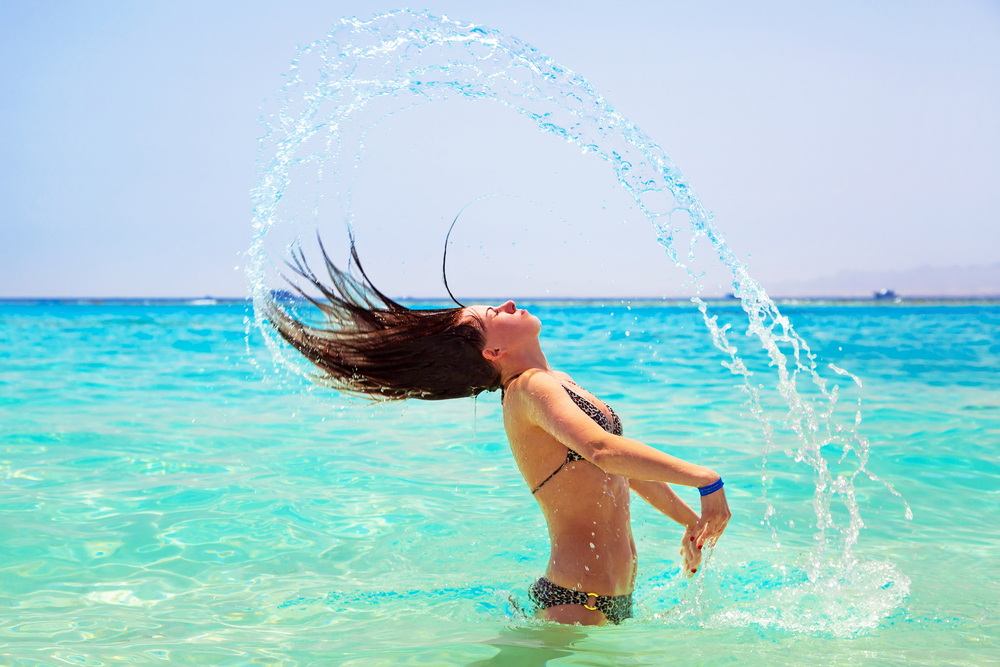 Mädchen im Meer an der Küste von Hurghada, sie trägt einen Bikini und wirft ihre nassen Haare in den Wind