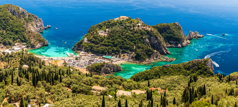 Paleokastritsa Bucht aus der Ferne mit türkisfarbenem Wasser, Hügeln und Parkplatz für Touristen