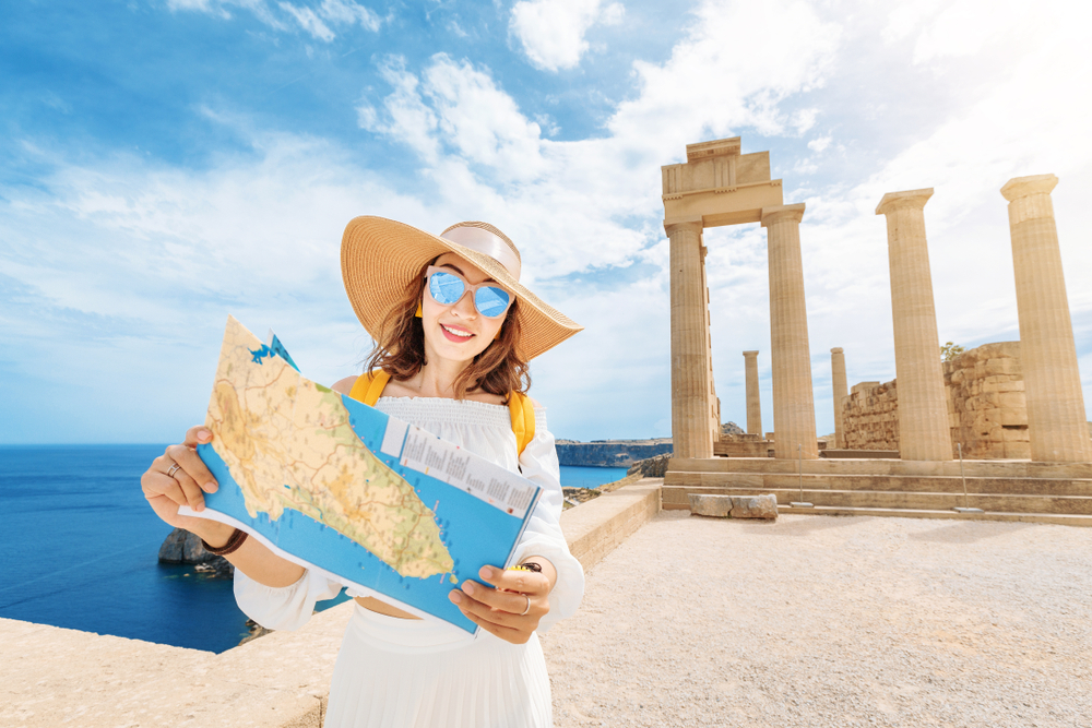 Besucherin vor der Akropolis von Lindos mit Landkarte, Sonnenhut und Sonnenbrille