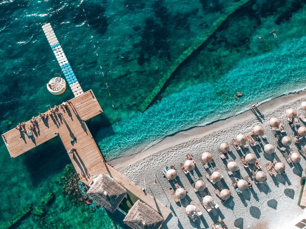 Vogelperspektive auf einen Strand in Bodrum mit Sonnenschirmen und Steg