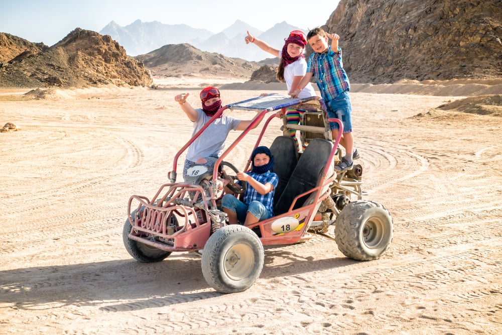 Vier Kinder bei einer Wuestensafari in Hurghada, alle Kinder posieren auf einem Strandbuggy