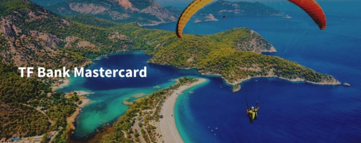 TF Bank Mastercard Schriftzug auf Bild von Strand mit türkisem Wasser aus der Vogelperspektive mit Paraglider
