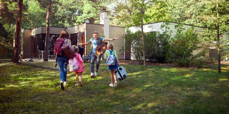Vater der seine Familie mit Frau und zwei Kindern vor einem Ferienhaus in einem Center Parc freudig begrüßt