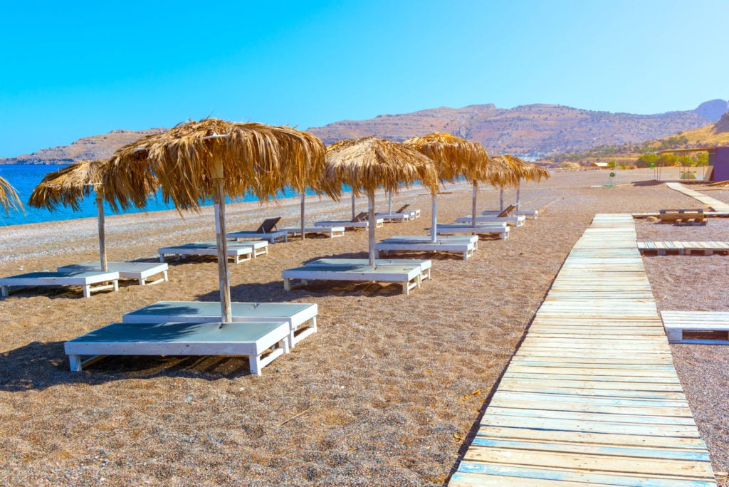 Holzsteg und Liegestühle mit Sonnenschirmen am schönen Strand von Kalathos. Rhodos, Griechenland