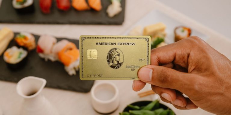 Goldene American Express Kreditkarte die in den Vordergrund vor ein Tisch mit Sushi Speisen gehalten wird
