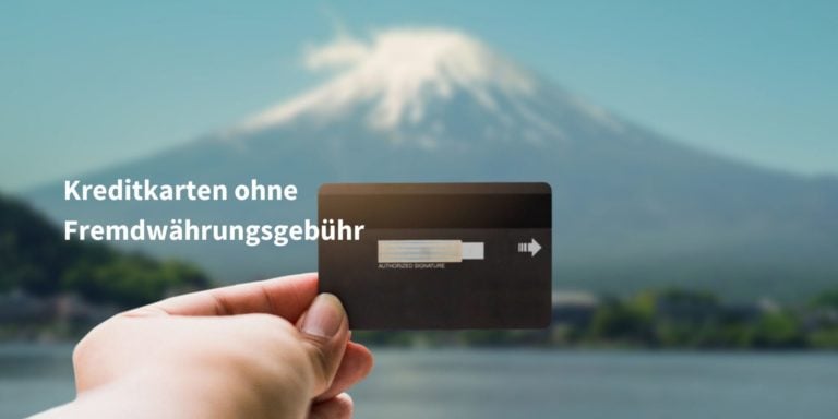 Schwarze Kreditkarte die von einer Hand im Vordergrund gehalten wird, im Hintergrund ist ein schneebedeckter Berg erkennbar.