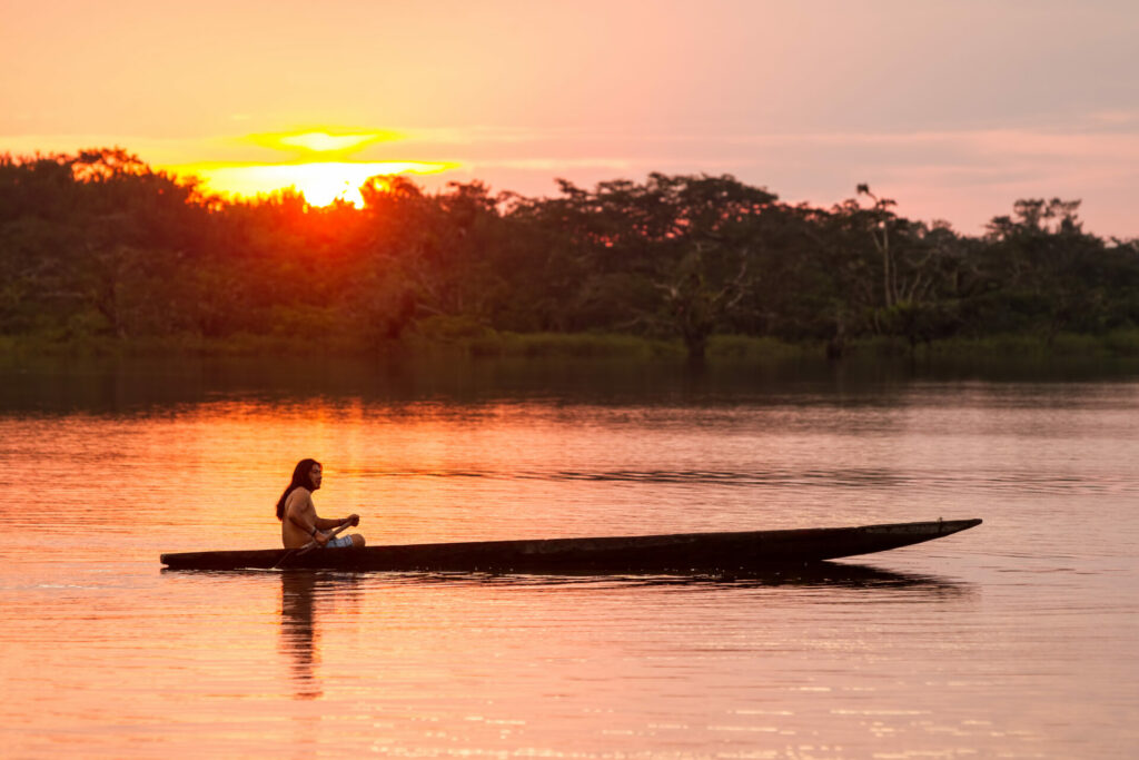 Indigender Mann fährt bei Sonnenuntergang mit dem Kanu