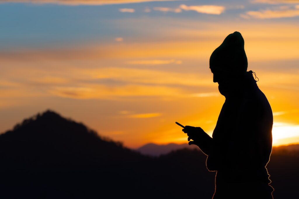 Silhouette einer Person zum Sonnenuntergang mit einem Smartphone